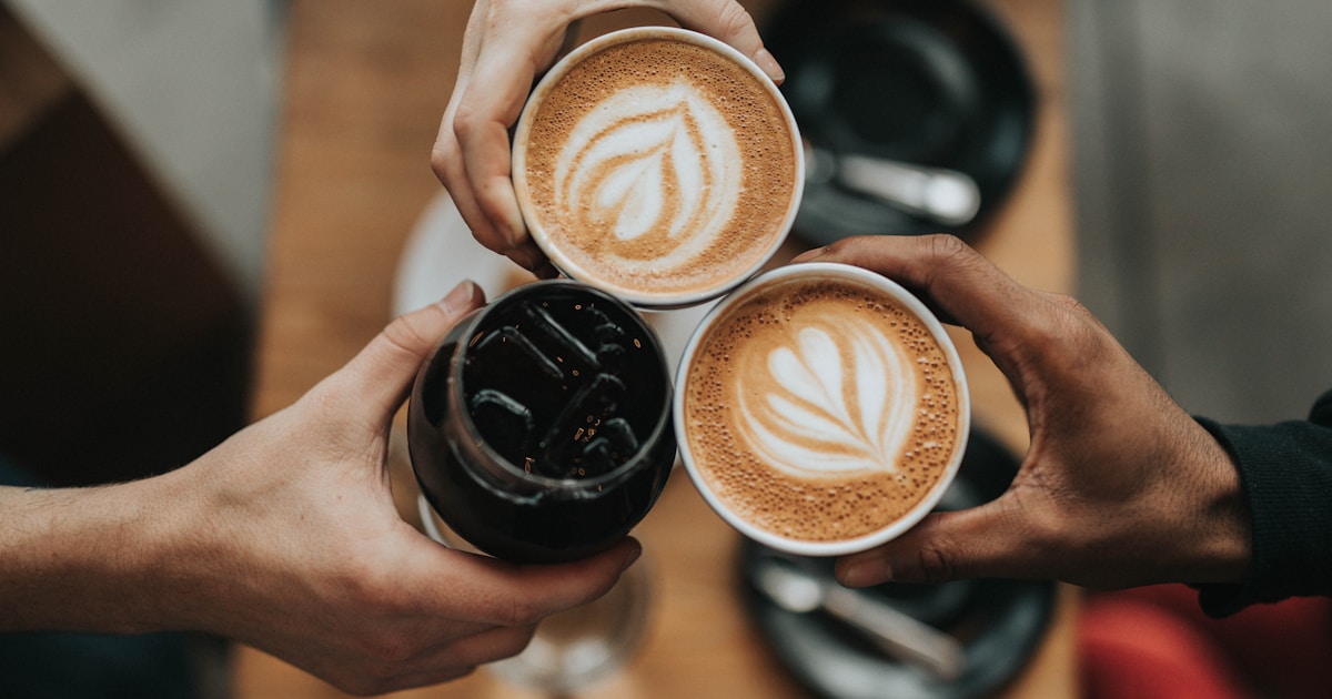 Three coffee mugs raised over a wooden table — a small reminder that the first month of sobriety is often kept together by ordinary mornings with other people