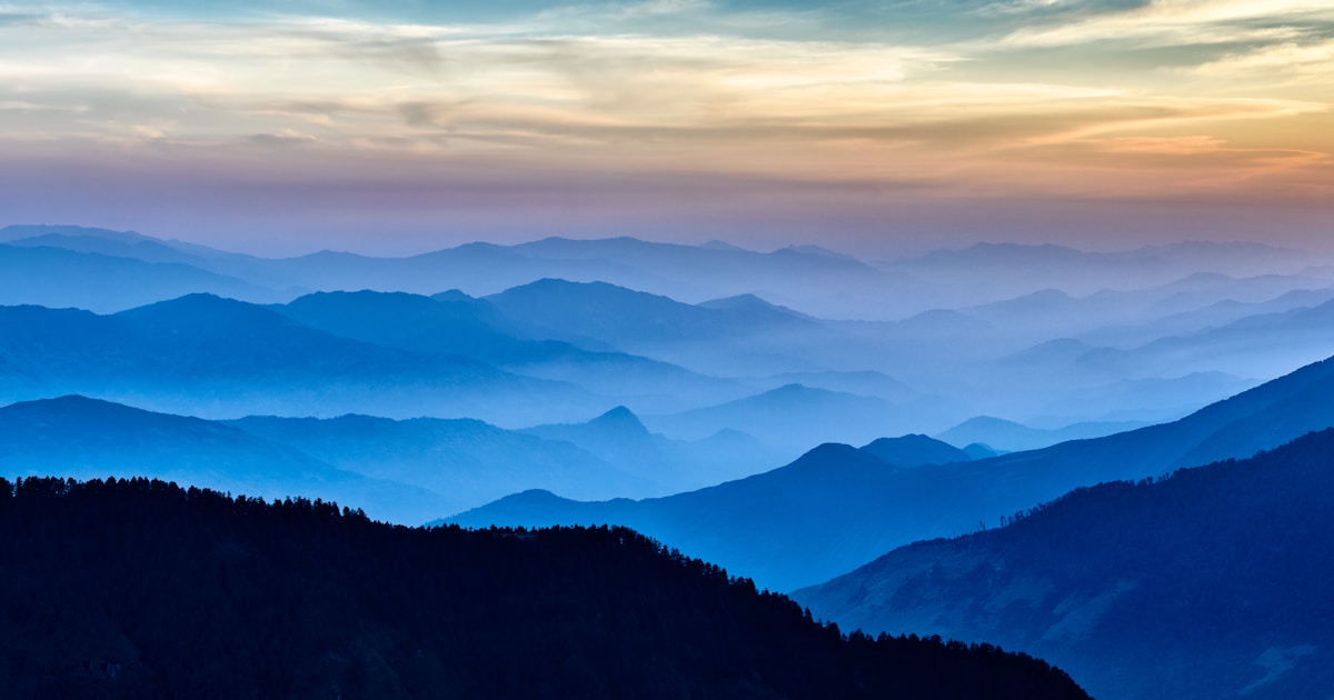 Layered blue mountain ridges with the warm last light of sunset on the horizon — relapse prevention strategies are the practices that protect the small flame of early recovery from the winds that put it out
